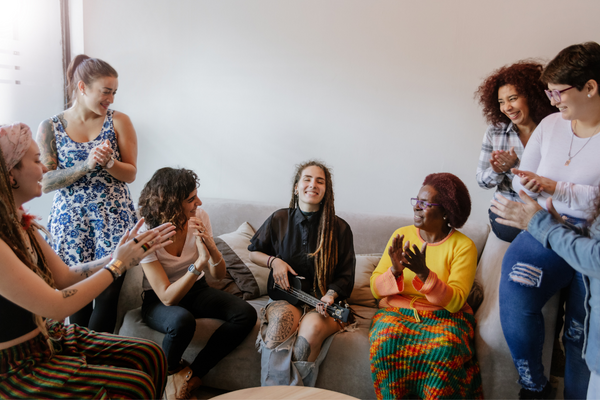 Group of seven women playing music and laughing together in a living room