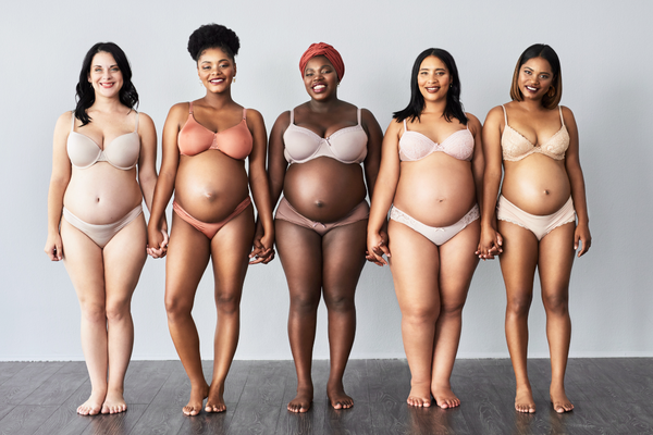 Five pregnant mothers from different races standing in underwear and holding hands