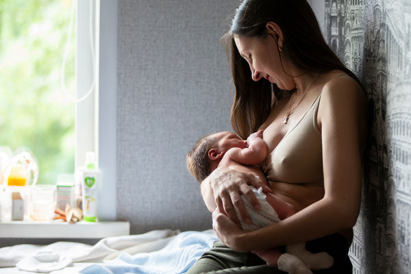 Mother breastfeeds newborn baby happily in front of a bright window
