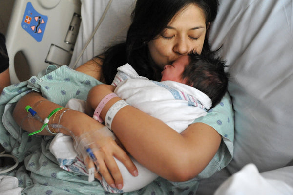 Mother kissing her newborn baby in the hospital bed