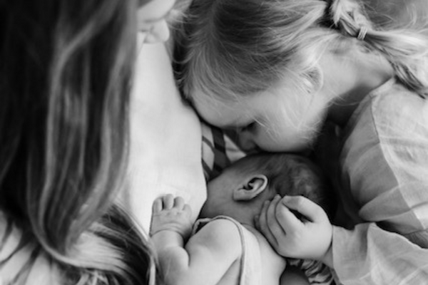 A girl kissing a baby’s forehead in black and white