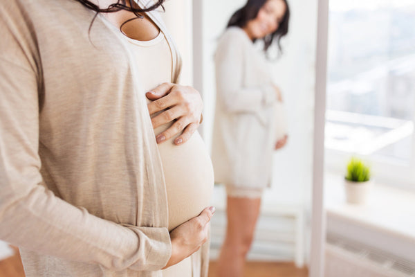 A pregnant woman is standing in front of a mirror and holding her stomach