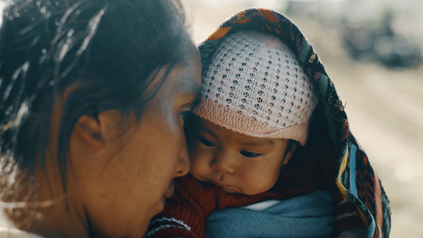 Mother nurtually holding her baby with a white crocheted hat and a blanket