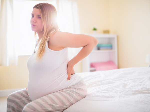 A pregnant woman sitting in a bed, experiencing discomfort due to pelvic pain