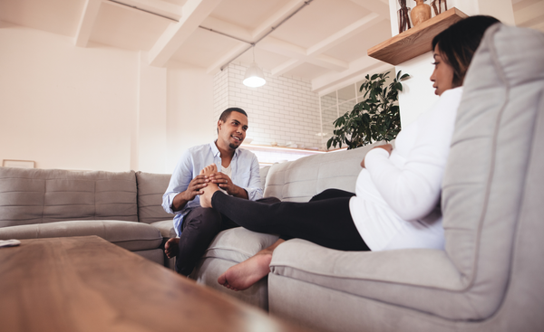 Man is massaging a pregnant woman’s feet on a sofa