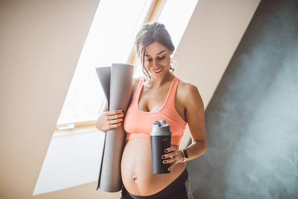 Confident pregnant woman with yoga mat and water bottle, prepared for an exercise session