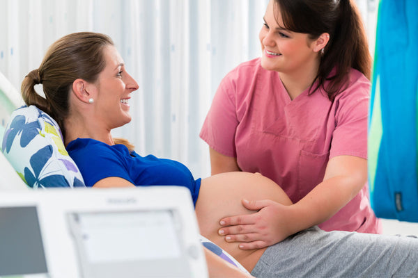 A pregnant smiling woman at the doctor’s office where nurse is holding her stomach