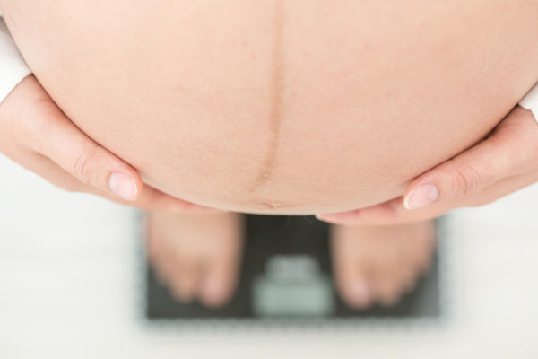 A close up of a woman holding her pregnancy stomach while stepping on a scale