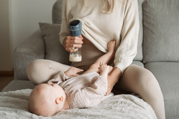 Mom is pumping breast milk while playing with her little baby