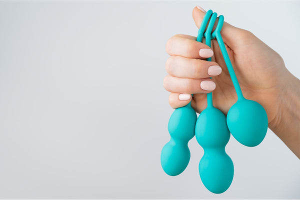 A woman's hand holding three distinct pelvic floor trainer Kegel balls of varying sizes