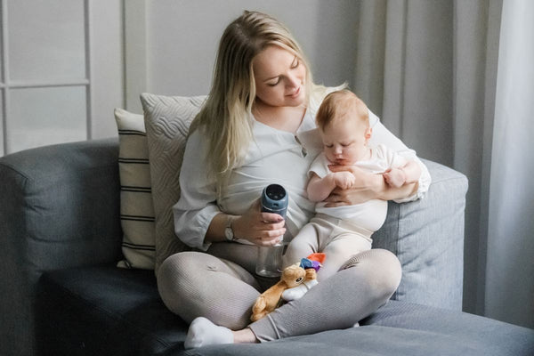 Mother pumping breastmilk with Lola&Lykke electric breast pump while  tenderly holding her baby
