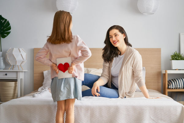 Little daughter hiding mother's day card for mother behind her back