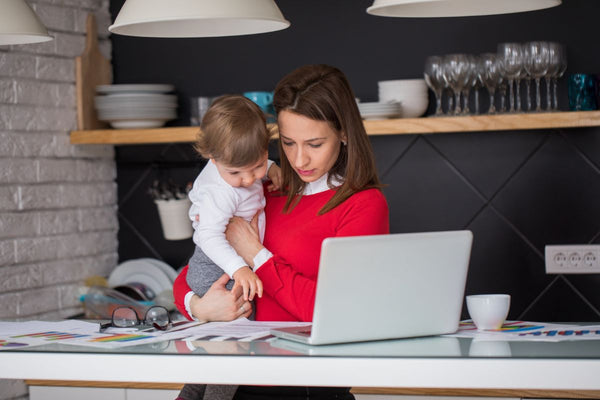 A women holding a baby and looking at papers and a laptop