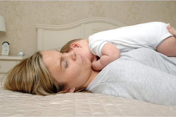 A woman laying on bed while holding a baby on her lap
