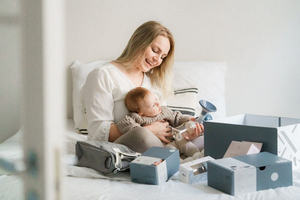 New mother with her baby, opening Lola&Lykke Breastfeeding Starter Kit on her bed