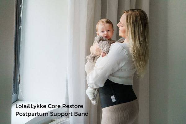Woman holding her baby while wearing a postpartum support band for abdominal comfort and recovery.