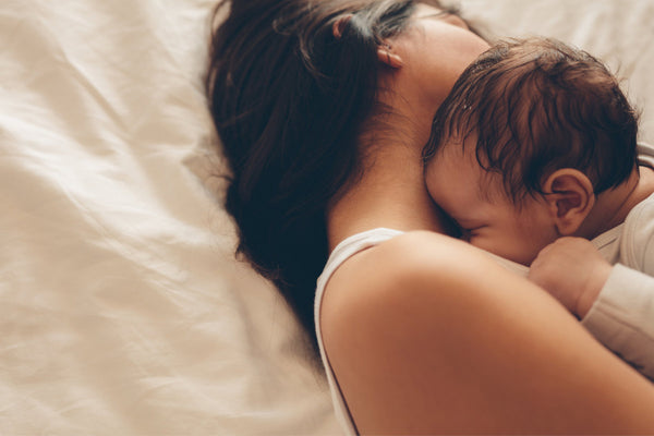 A pregnant woman with siblings, lying on a bed while holding her baby