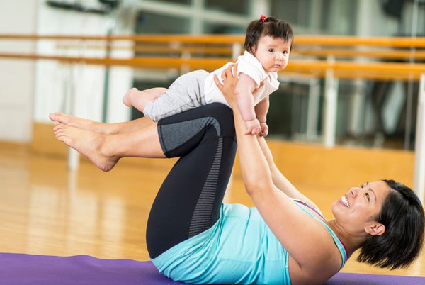 A mother engaging her abdominal muscles after pregnancy through gymnastics, joyfully involving her baby in the activities