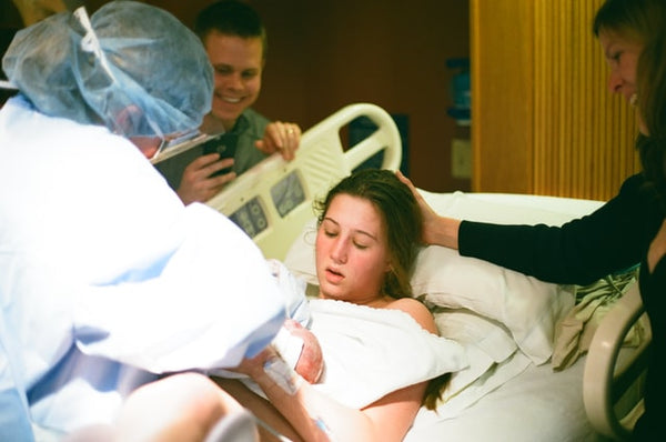 A mother is holding her newborn baby at a hospital while midwife is helping her