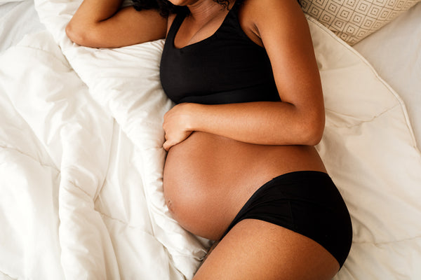 A pregnant woman is laying in bed on her side
