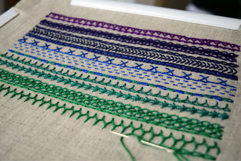 Embroidered band sampler with lines of stitches in shades from purple to deep green