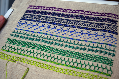 Hand embroidered band sampler in shades ranging from purple to lime green 