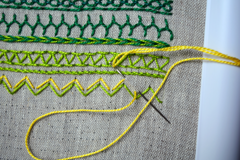 Embroidery band sampler in greens and yellows with arrowhead stitch in progress