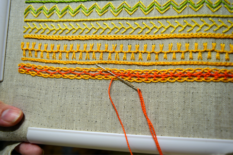 Embroidery band sampler in yellow and orange with interlaced cable chain stitch in progress