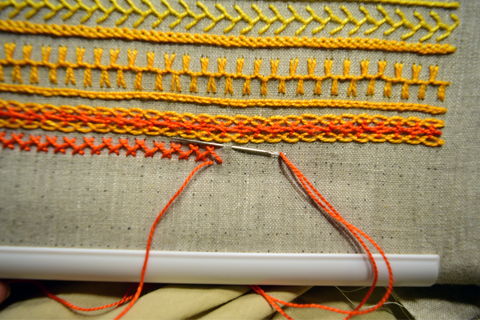 Embroidery band sampler in yellow and orange with herringbone stitch in progress