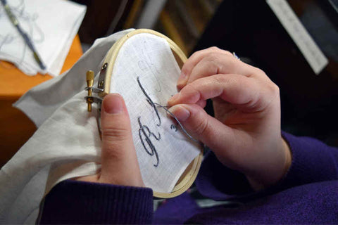 Closeup shot of a woman's hands (Jen's) holding embroidery hoop with work in progress, monogram R B in progress on corner of handkerchief