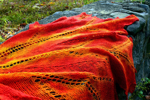 Handspun leaf shawl in brilliant reds and golds, draped over rock wall