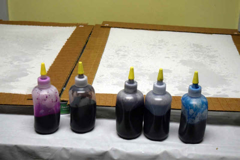 White silk stretched in frames, with bottles of dye in blue, purple, and pink in front ready to begin dyeing