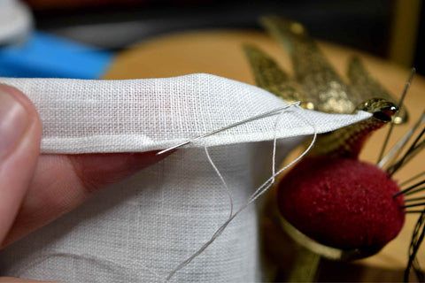 Creating a hand-rolled hem on white linen using the help of a sewing bird