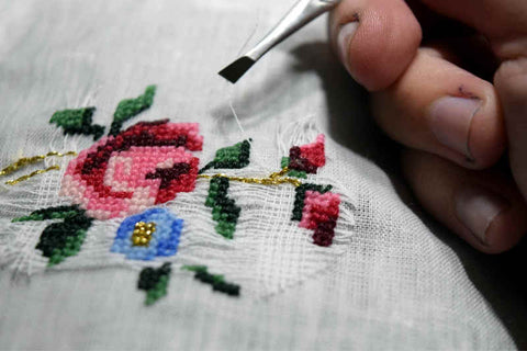 Cross stitch rose design finished, hand with tweezers removing waste canvas from underneath stitching