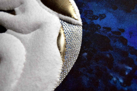 Detail of white felt and gold kid leather padded embroidery on handpainted blue silk ground. An arc of the background is filled with silver threads smoothly tacked down with shades of blue silk.