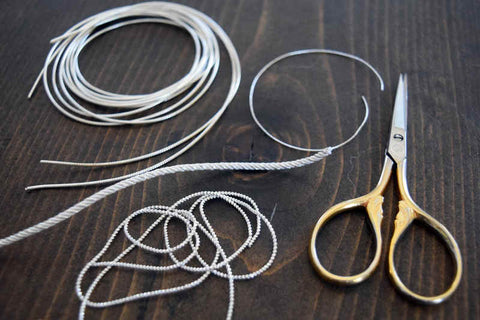 Silver metal thread of various styles and scissors laid out in preparation for metal thread embroidery
