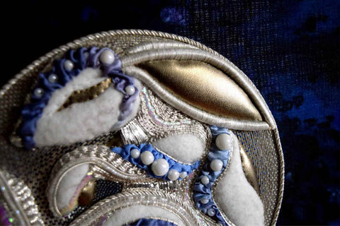 Silver and blue rabbit being embroidered in silver circle on blue ground; rabbit's front half is visible and in progress using several different metal threads for texture.