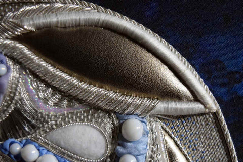 Close up of rabbit ear in progress using goldwork embroidery; inner ear is smooth golden leather and outer edge of ear is silver worked in a pattern of bright and smooth metal threads