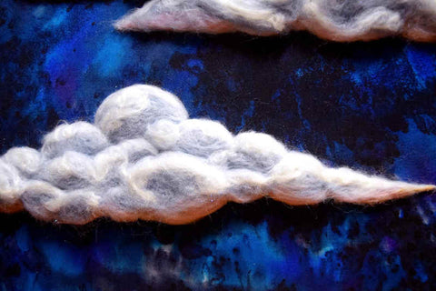 A cloud worked in wool in white, blue and pink; it appears to float over the dark blue background with the last rays of sun pinking the bottom and the moon silvering the top edge.