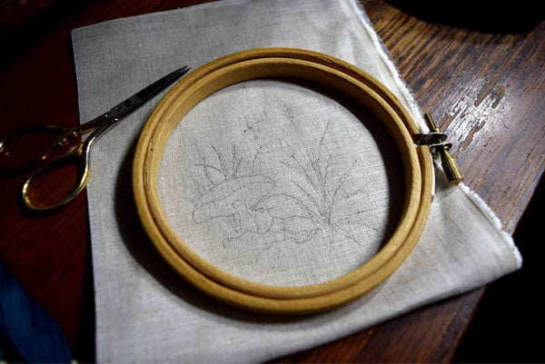 Embroidery hoop and natural color linen, lightly traced with design of mushroom and grass