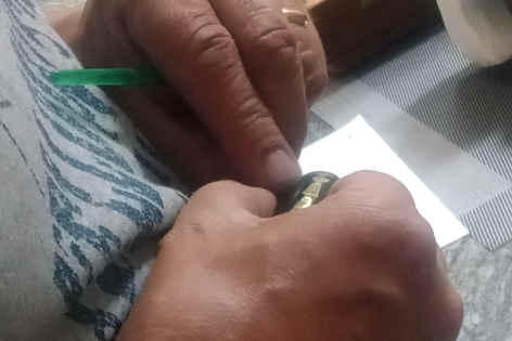 Closeup of a man's hands holding a piece of black enamelled metal with a glimpse of golden design visible