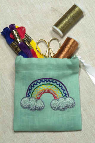 Small drawstring pouch with embroidered rainbow on front in bright colors and multiple stitches, filled with embroidery supplies