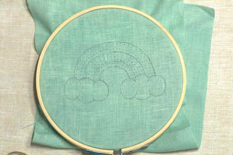 Green fabric in embroidery hoop marked with rainbow design and ready to be embroidered
