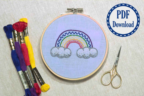 Finished rainbow sampler tutorial piece framed in hoop with scissors and thread alongside. Rainbow worked in series of stitches and pdf download stamp in corner.