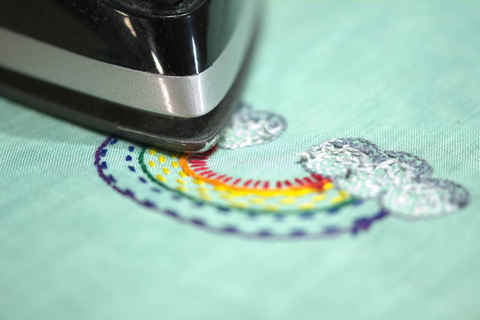 Photo of iron pressing backside of embroidered rainbow in bright colors