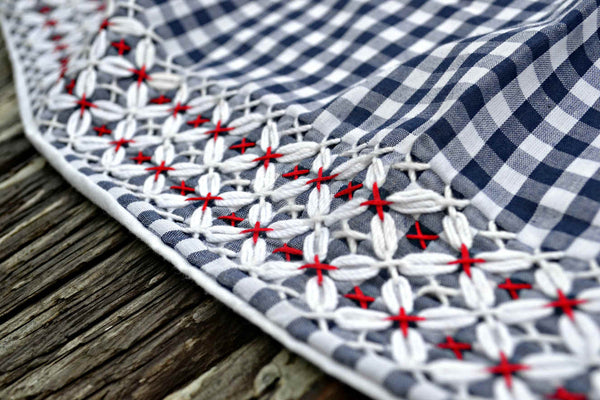 Gingham apron hem in blue and white check, embroidered with blue, red, and white chickenscratch design