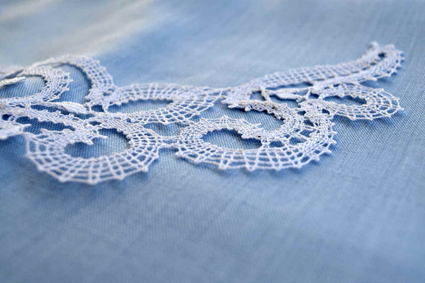 Vologda white lace necklace, shown from the side close up on pale blue linen