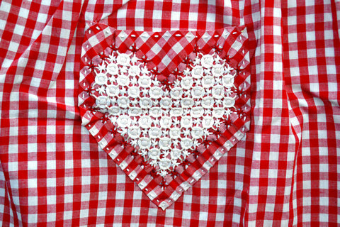 Detail of red and white gingham apron, showing chickenscratch heart design on pocket