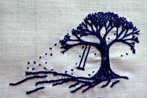 Navy tree with rope swing embroidered on white linen; leaves are falling from it in an imagined breeze