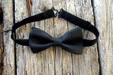Black Irish linen bow tie adjustable and pre-tied, resting on weathered wood